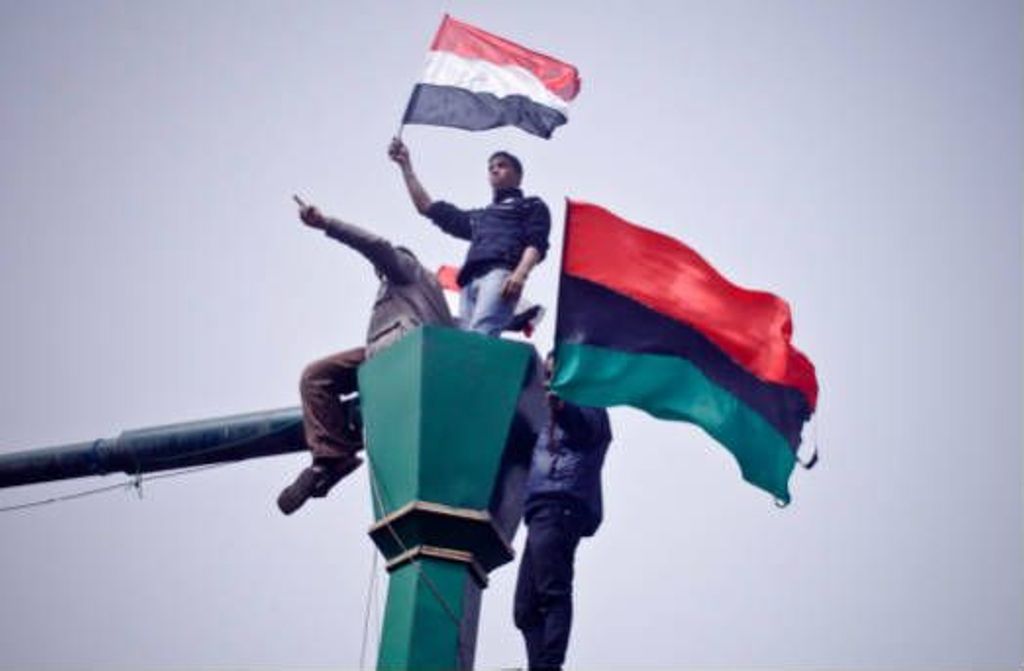 Miniature of Demonstrators on a lammpost waving Egyptian and Libyan flags